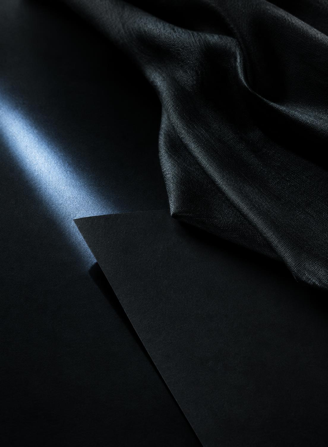 Temporary editorial placeholder: charcoal fabric and paper with a blue edge light